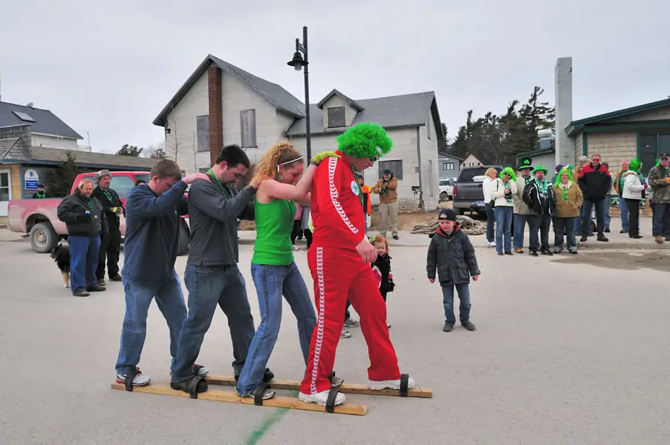 Four people move together on wooden planks while spectators watch along a street.