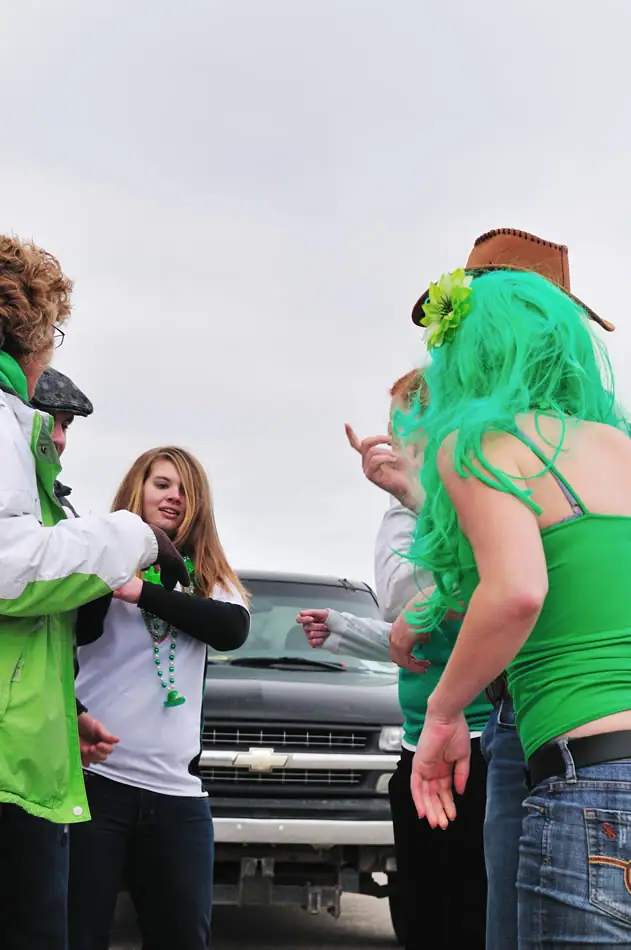 People in green-themed clothing gather outdoors in front of a Chevrolet truck.