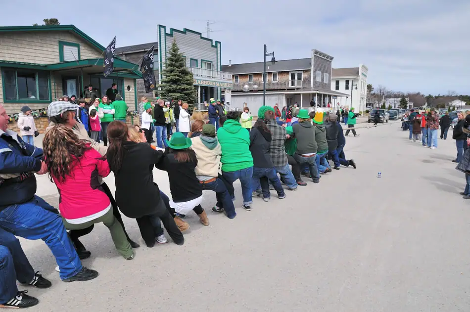 A tug-of-war unfolds on a street as spectators watch near storefronts.