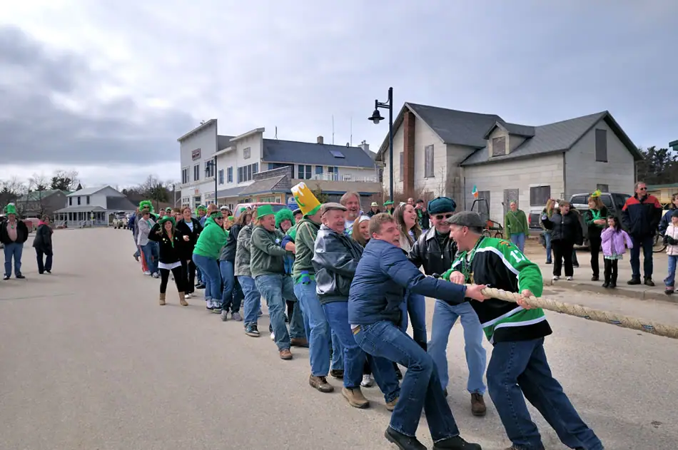 Participants pull a rope in a tug-of-war on a paved street while spectators watch.