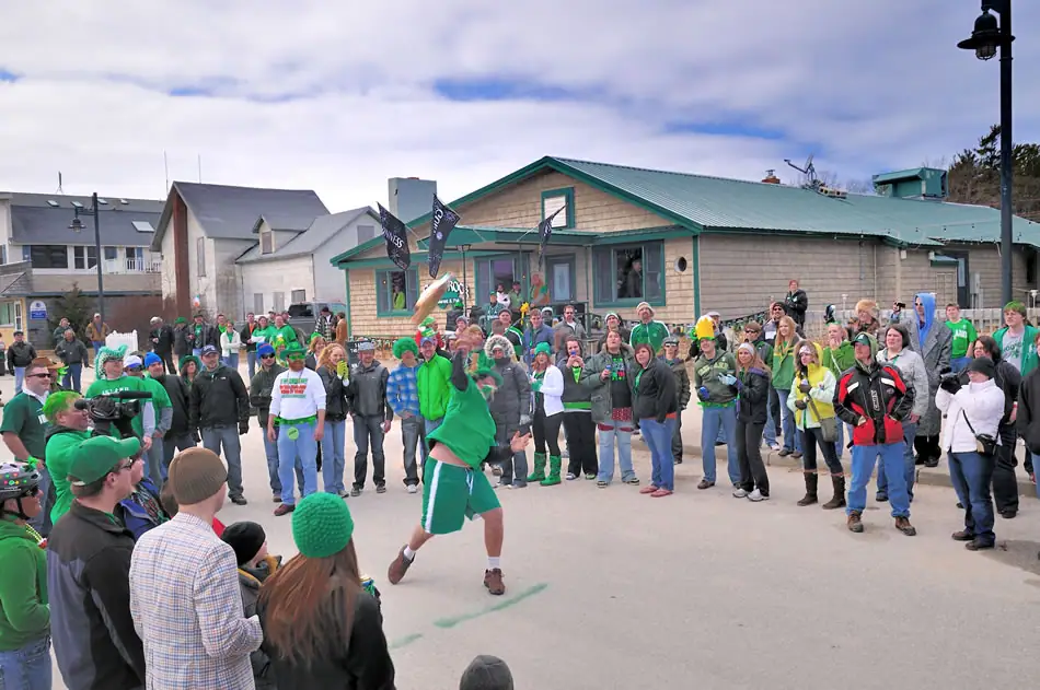 A crowd watches a man in green athletic clothing throw a bottle-shaped object outdoors.