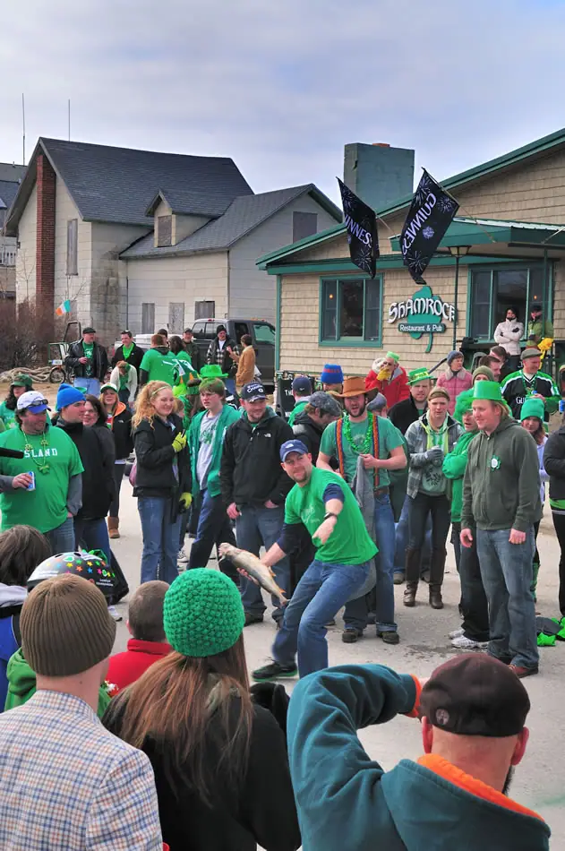 Crowd in green gathers outside a pub as a man holds a fish.
