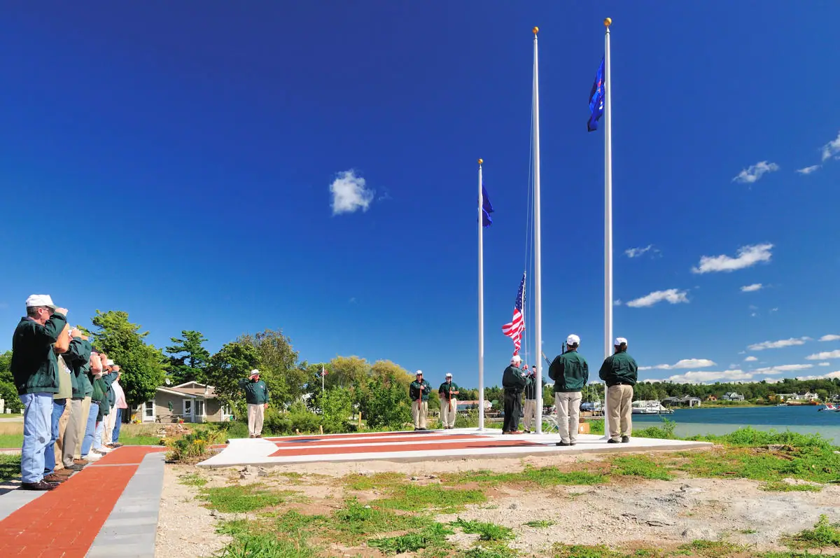 People salute during a flag-raising ceremony beside a waterfront memorial platform.
