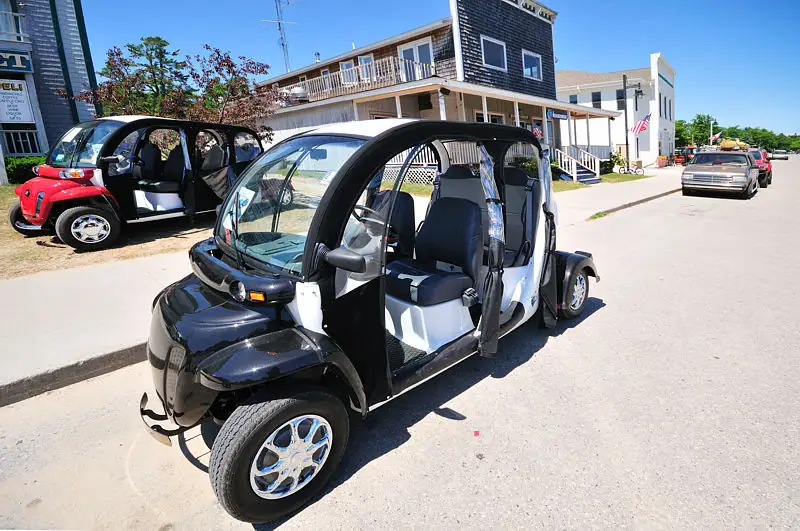 Black-and-white golf cart displayed on a sunny street beside buildings and another golf cart.