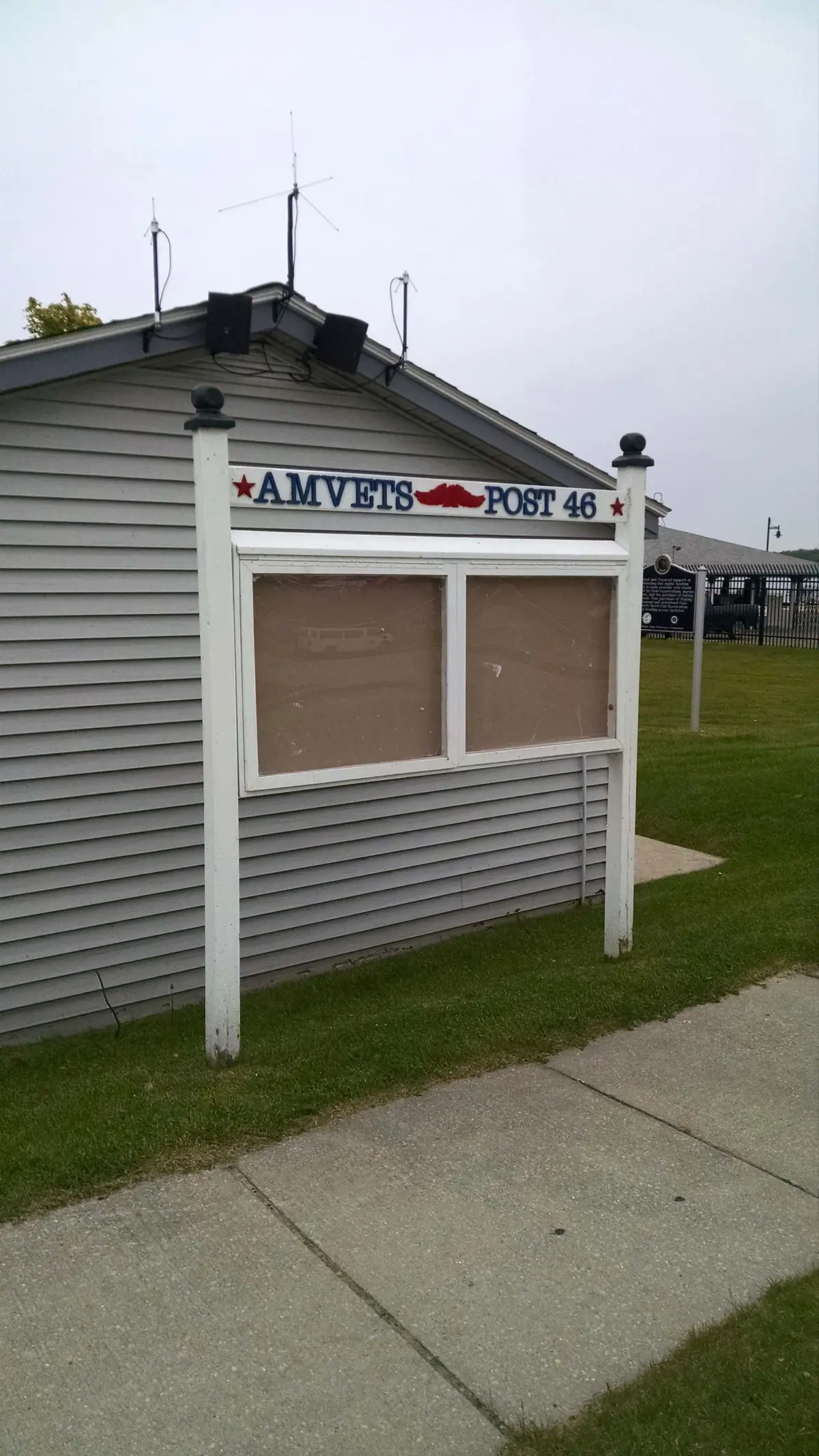 A pair of empty bulletin boards stands beside a light-sided building, beneath a sign reading “AMVETS POST 46.”