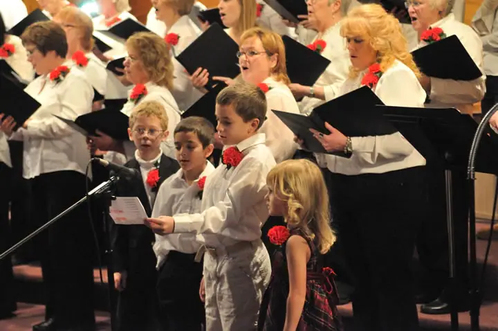A choir and several children sing together while holding music folders and sheet music.