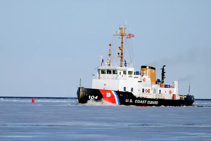A Coast Guard vessel marked 104 moves through ice beside a red buoy.