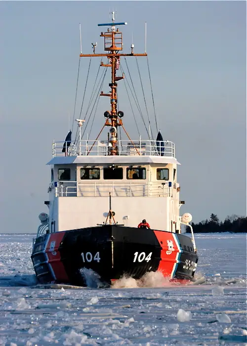 An icebreaker marked 104 pushes through broken ice with a person standing on its bow.