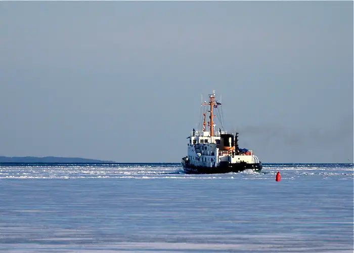 A tugboat moves through broken ice past a red buoy.