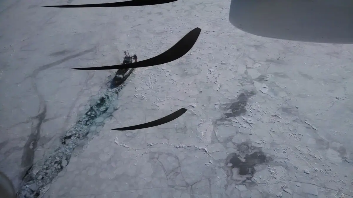 A vessel moves through a narrow open-water channel surrounded by ice, seen from above.