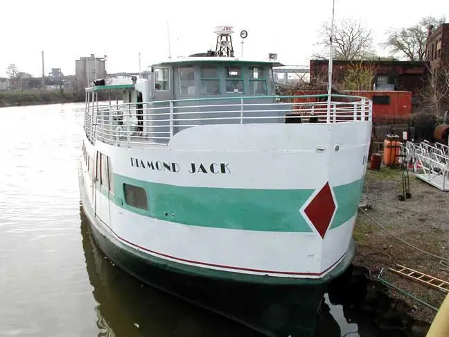 A white-and-green tugboat named DIAMOND JACK is moored beside an industrial waterfront.