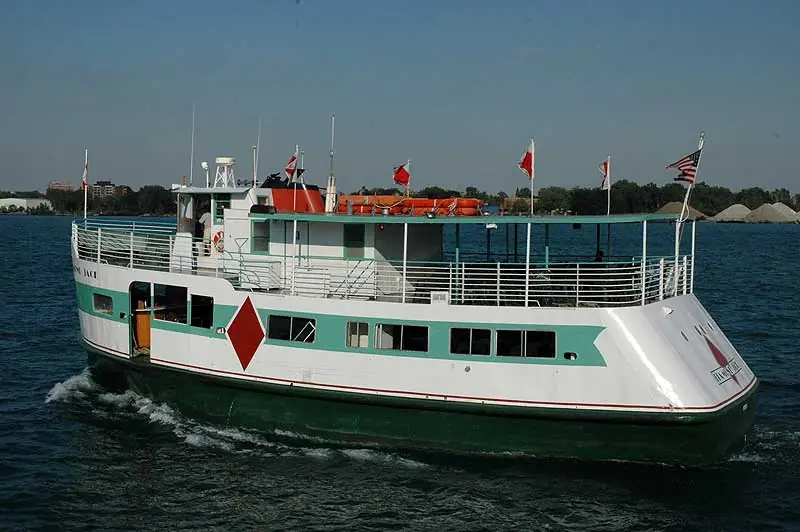 A white-and-teal passenger ferry moves through dark water with flags flying from its decks.
