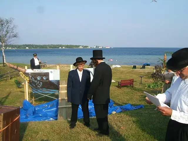 Outdoor ceremony with people in period clothing beside a waterfront display.