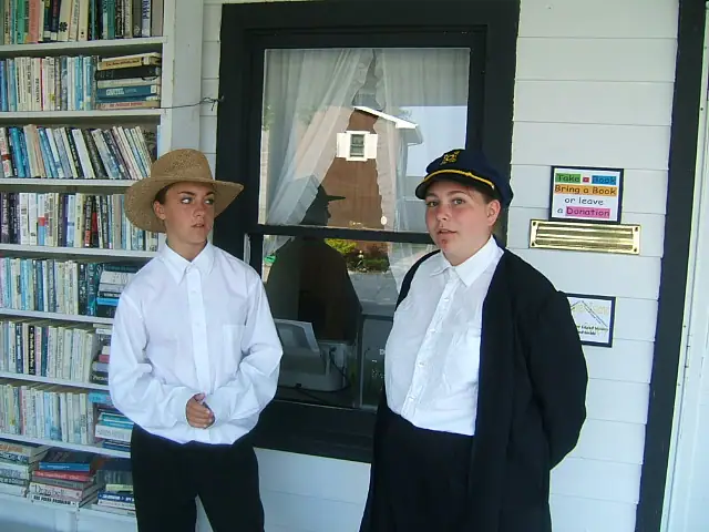 Two young people stand beside a book exchange shelf and a window displaying a donation sign.
