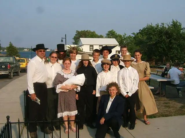 A group in period-style clothing poses beside a waterfront walkway and wrought-iron fence.