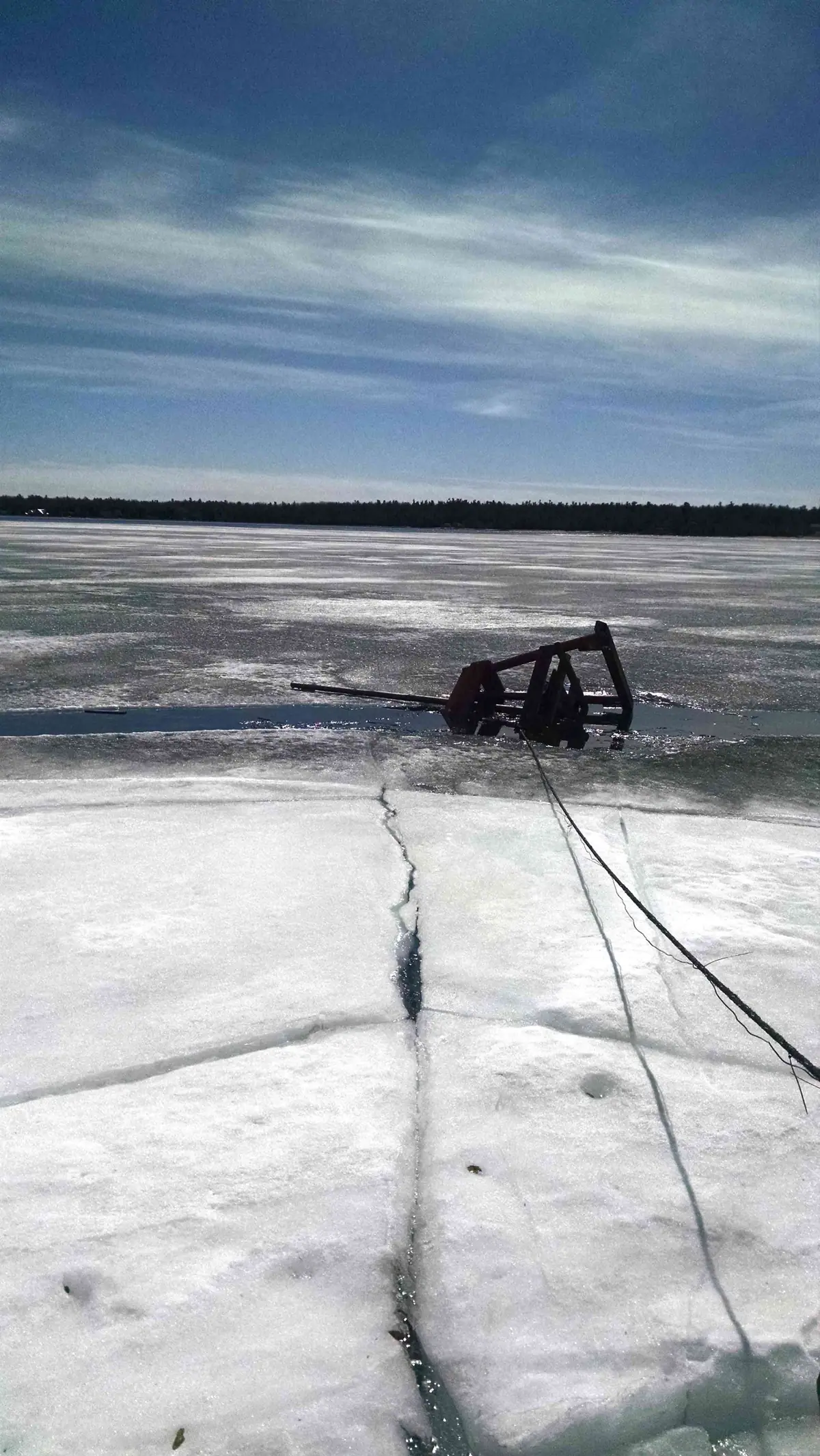 A red metal apparatus rests on cracked, snow-covered ice, with cables stretching toward the foreground.
