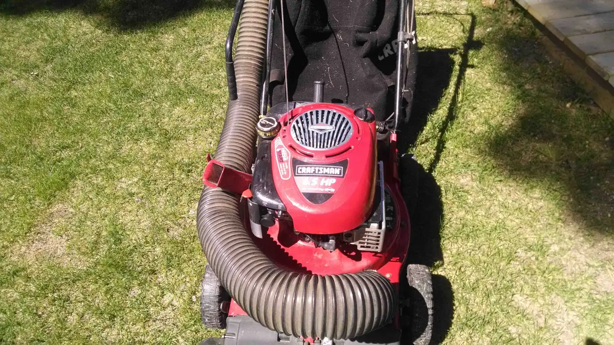 Red lawn vacuum with a large corrugated hose on a grassy lawn.