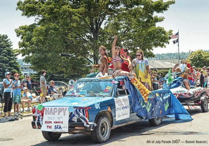 A blue pickup truck decorated as an undersea-themed parade float, surrounded by people and spectators.