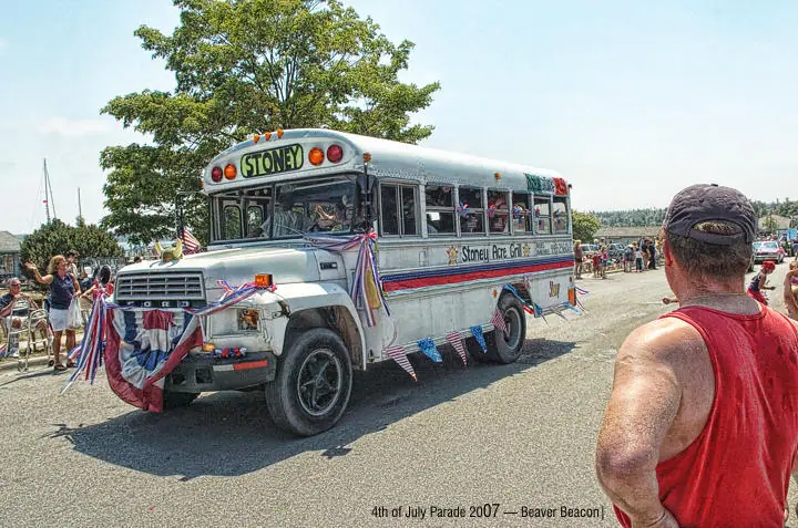 A decorated bus moves through a parade as spectators watch from both sides of the street.