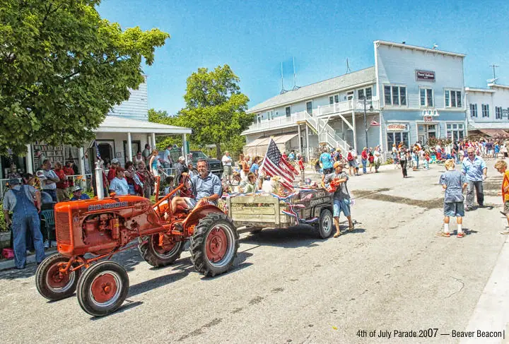 A red tractor pulls a decorated trailer through a crowded street parade.