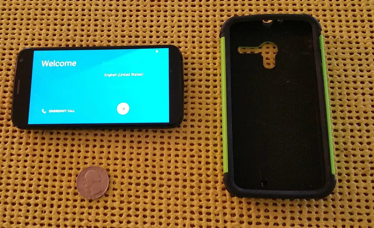 Two mobile phones and a coin rest on a yellow woven surface; one phone shows a welcome screen.