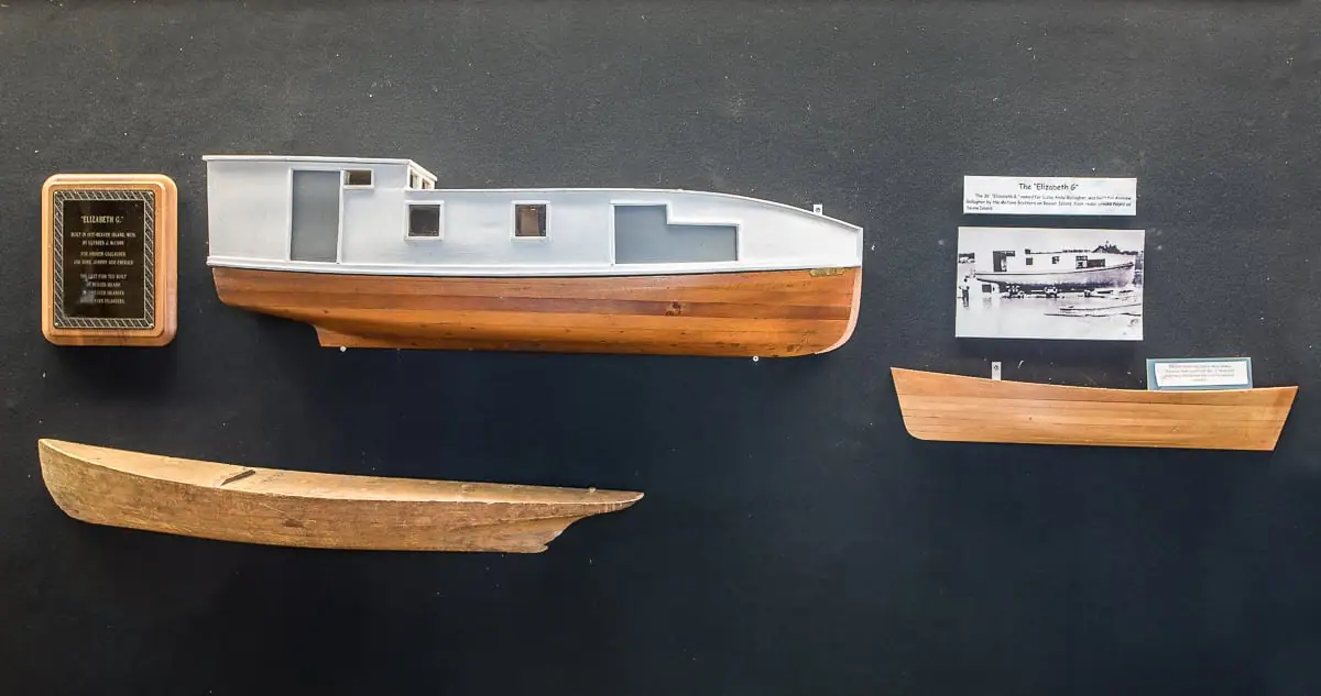 Museum display featuring a wooden cabin boat model, additional hulls, photographs, and informational plaques.