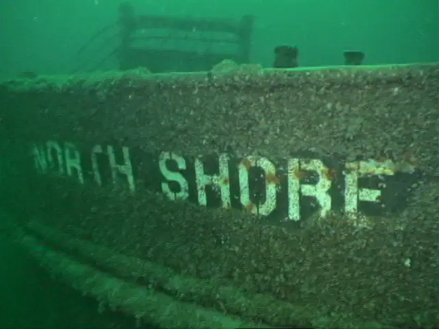 Close view of a dark, heavily encrusted hull with large painted lettering reading “NORTH SHORE.”
