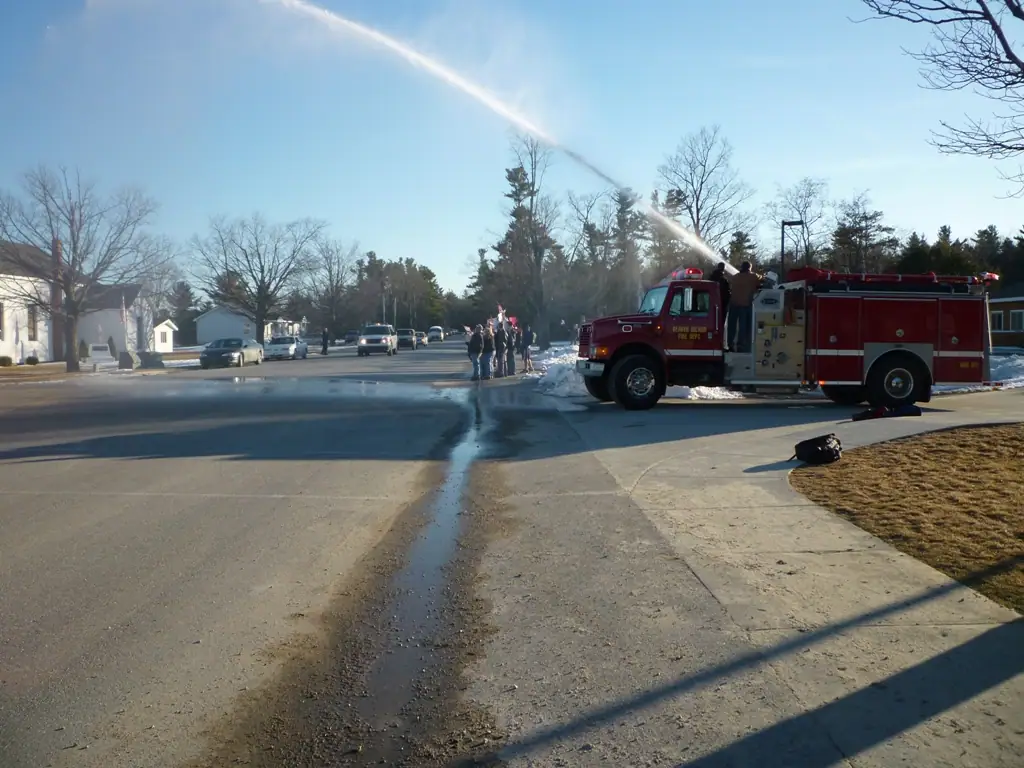 A red fire truck sprays water across a snowy residential street while people watch.