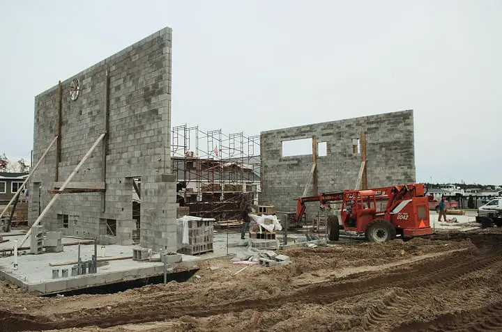 Concrete block walls, scaffolding, and a red loader fill a muddy construction site.