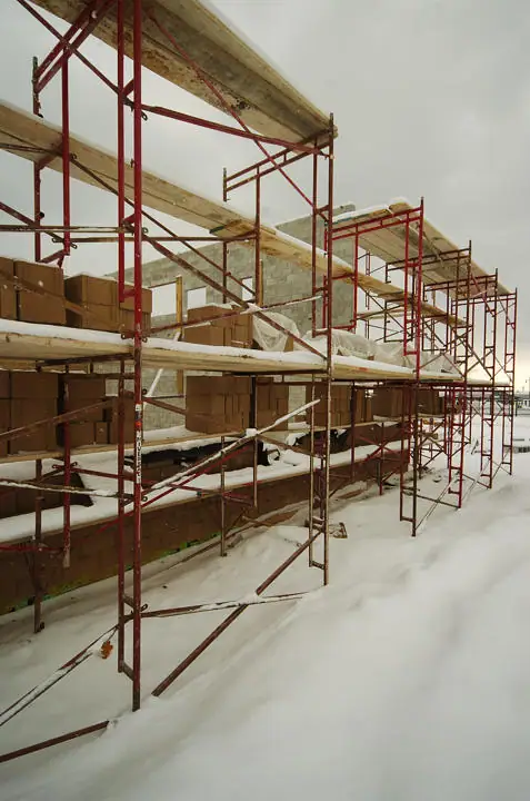 Snow-covered scaffolding and masonry walls at a building construction site.