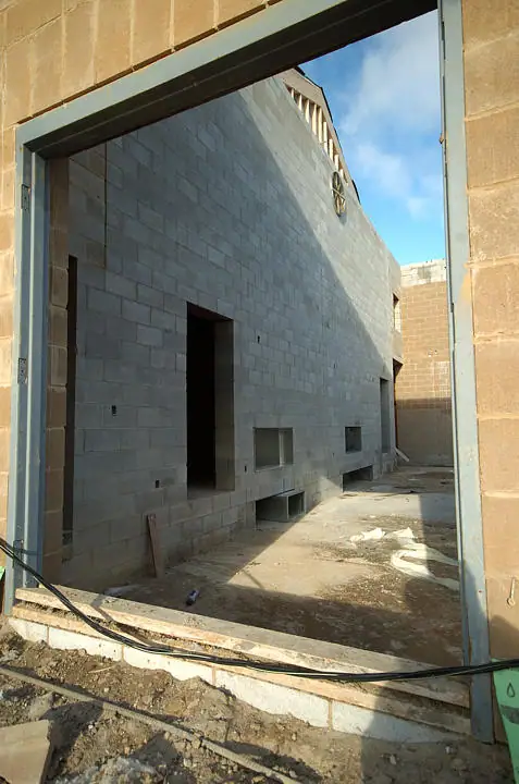 View through a metal-framed opening toward an unfinished concrete-block building and construction debris.