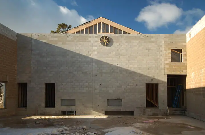 Unfinished building interior with concrete-block walls, timber roof framing, and a circular window.