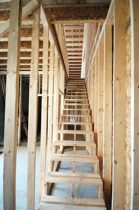 Unfinished wooden staircase inside a building with exposed wall and ceiling framing.