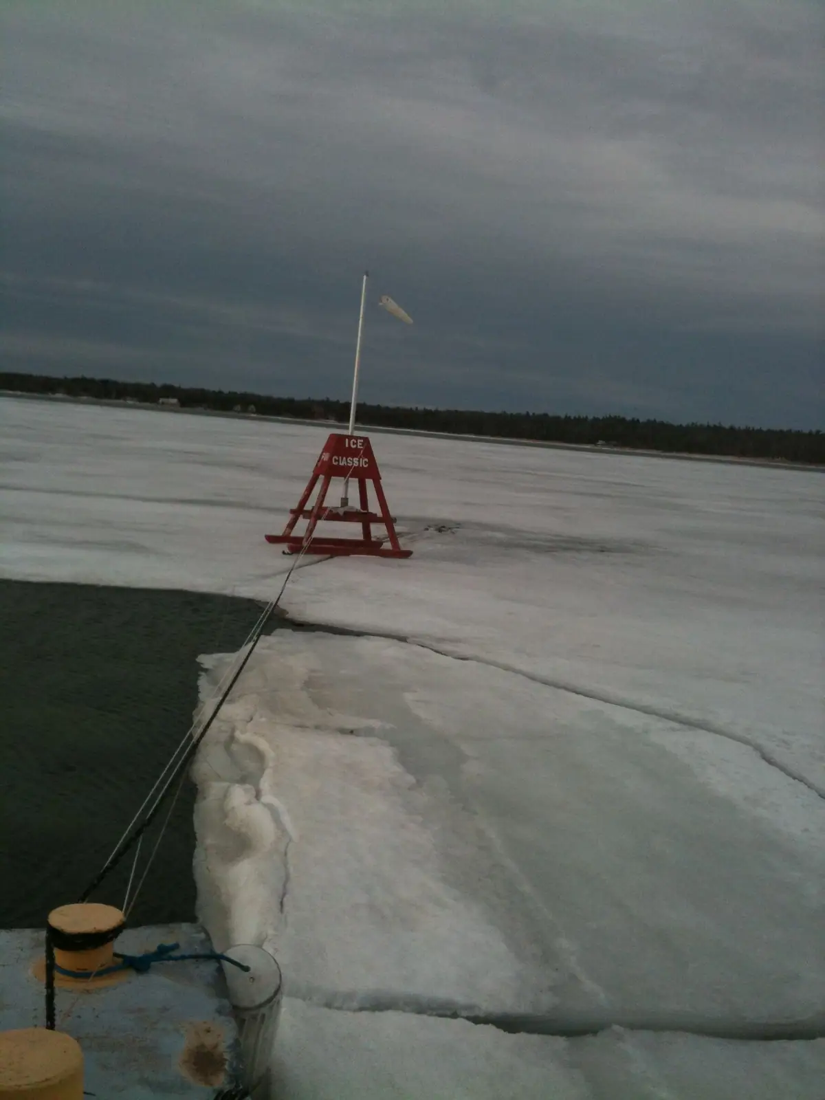 A red A-frame marker labeled “ICE CLASSIC” stands on frozen water beside an open channel.