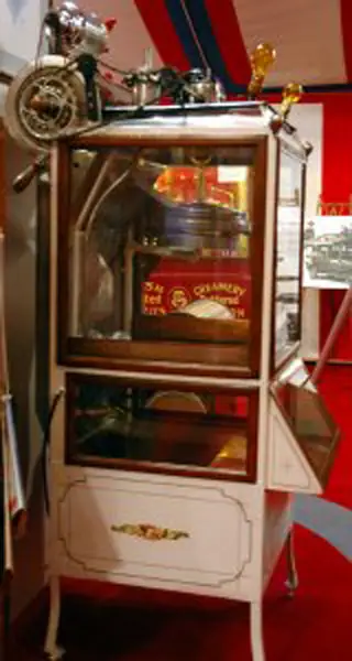 A tall glass-fronted display cabinet holds a small motorcycle and a red package marked “CREAMERY.”