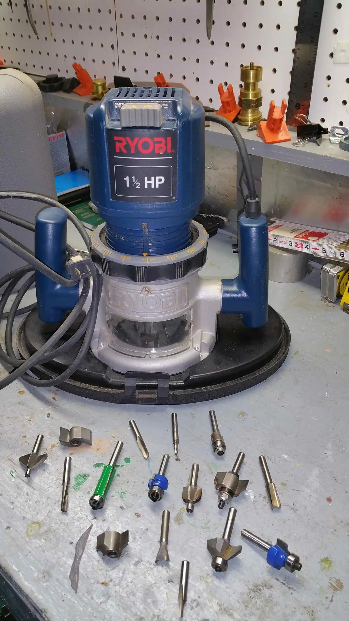A blue-and-silver power router stands on a workbench among router bits and workshop tools.