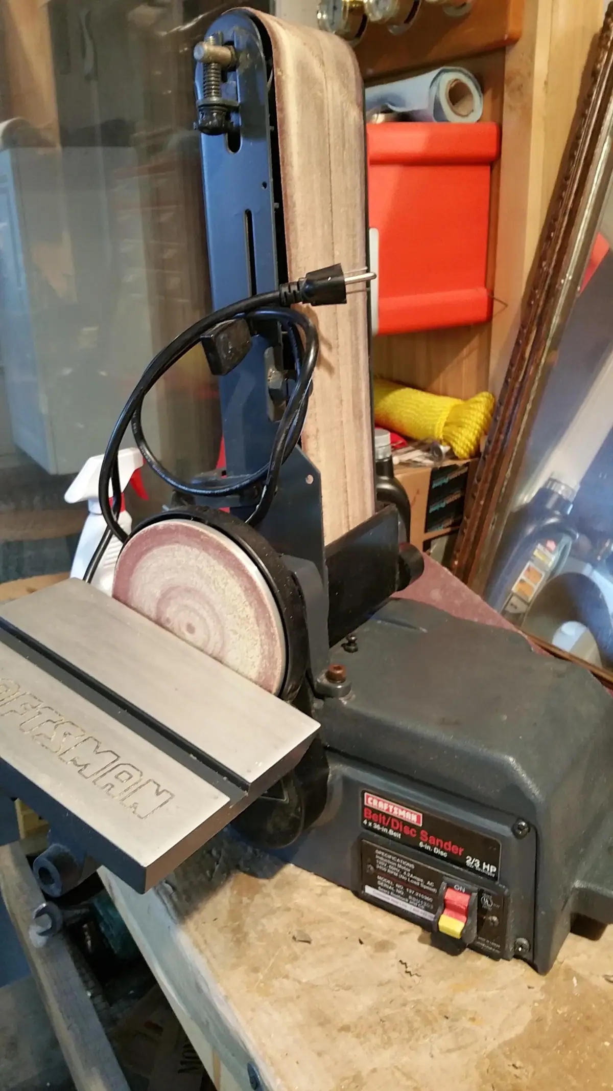 A benchtop belt-and-disc sander with a sanding belt, disc, power cord, and control switches.