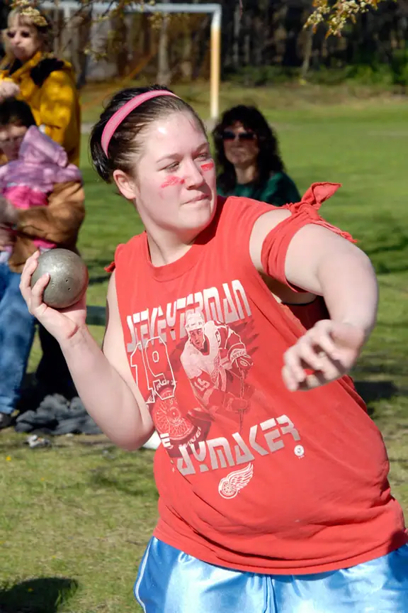 Athlete holding a shot in preparation for a throw, with spectators seated behind her.