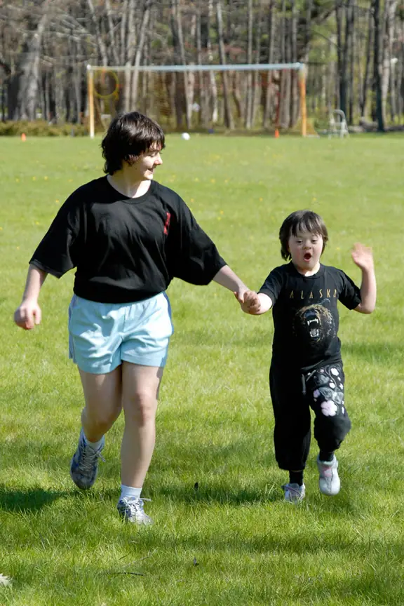 An adult and child run hand in hand across a grassy field.