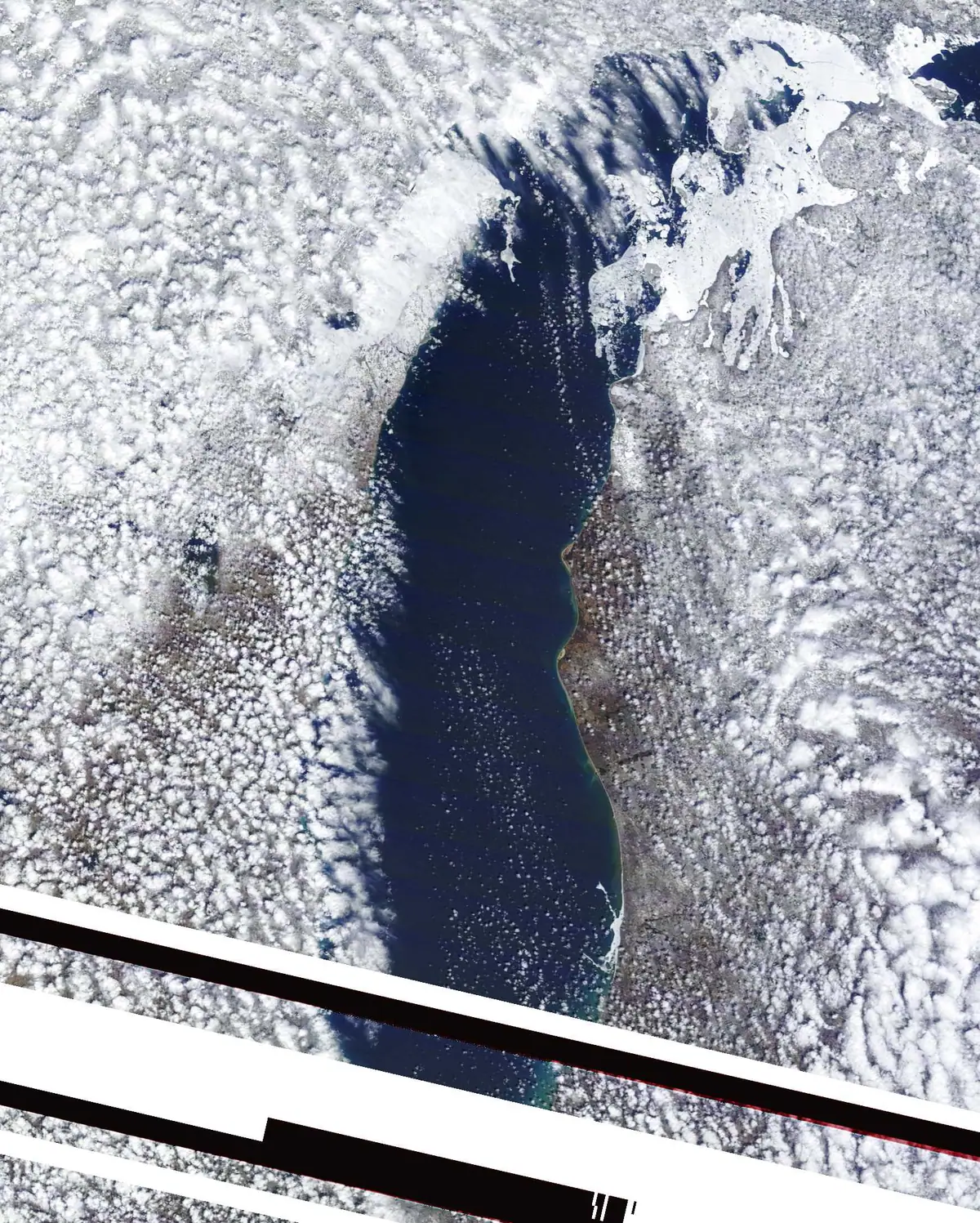 Aerial photograph of dark water, broken ice, snow-covered land, clouds, and diagonal aircraft structure.