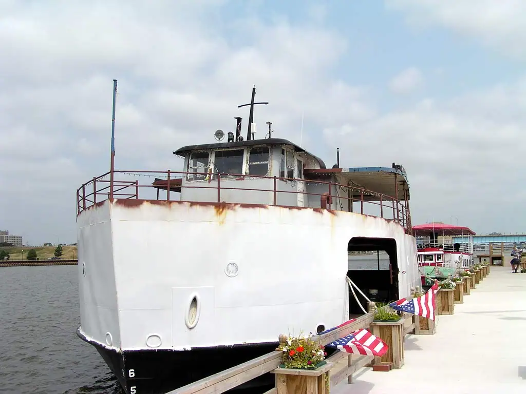 A large white ferry sits beside a decorated pier, with a smaller red-canopied boat behind it.